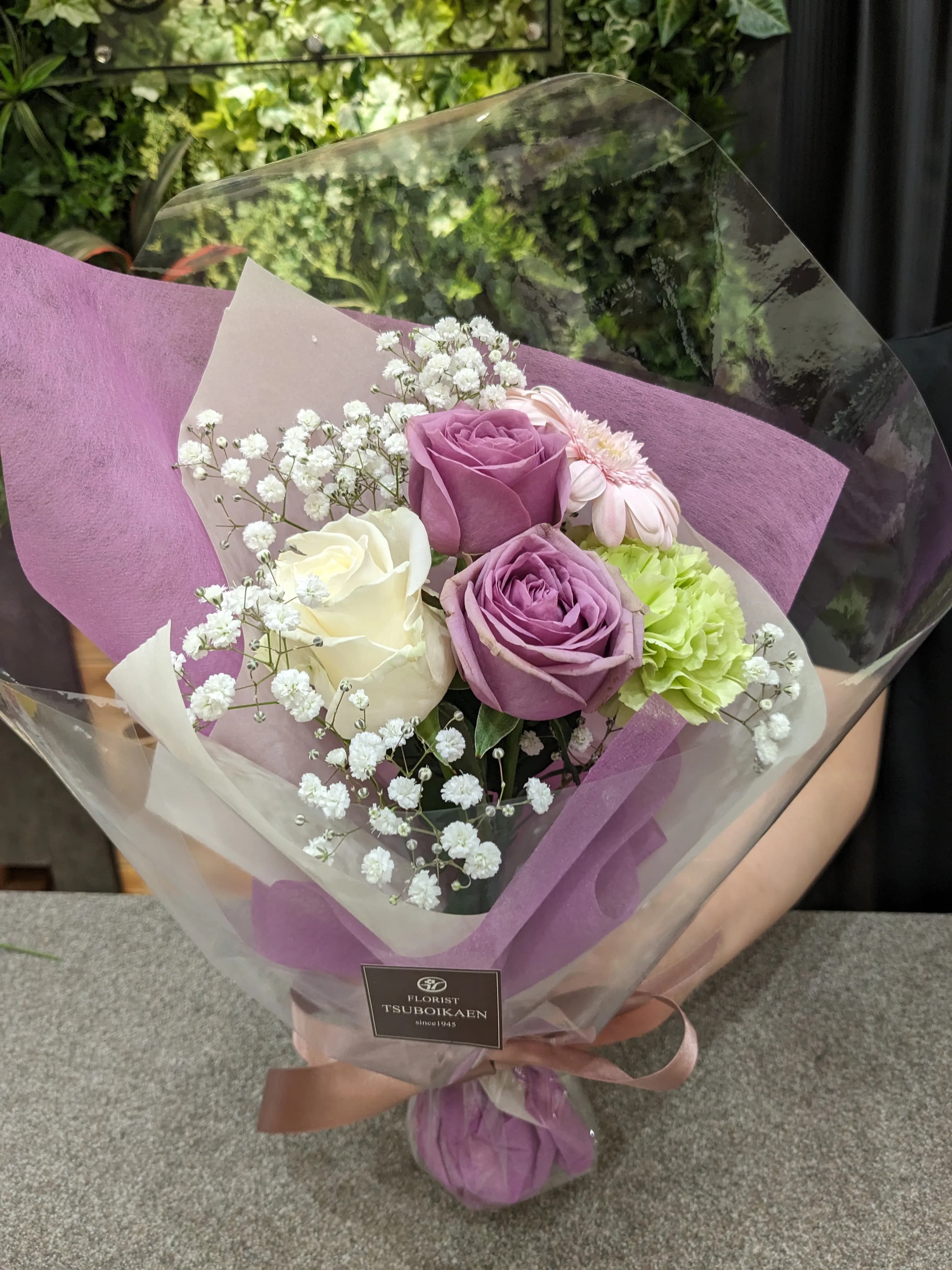 ピンクと白と薄緑の花を薄紫の紙でラッピングした上品な花束