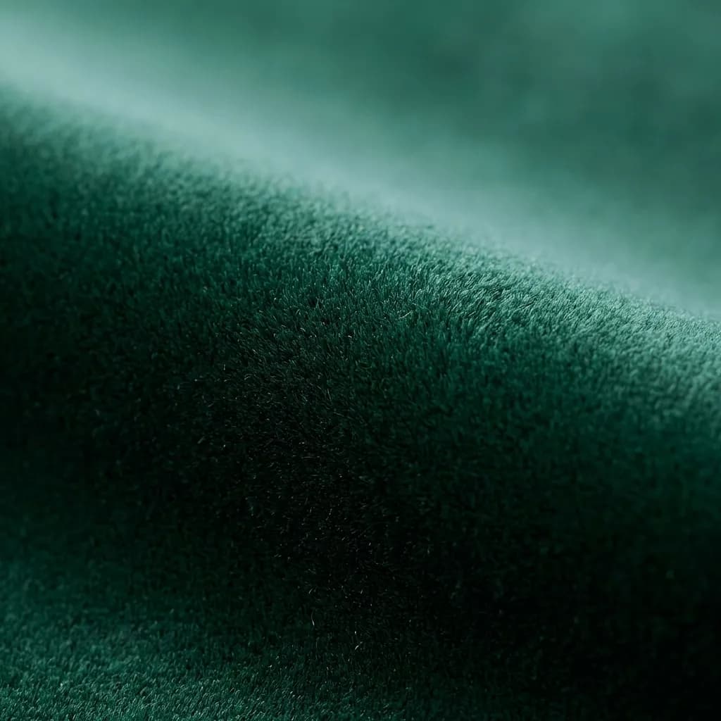 深みのあるエメラルドグリーンのベルベット生地を捉えた、贅沢で触感豊かなクローズアップ写真です。柔らかく起毛した生地は光を美しく反射し、緩やかな曲線やひだの上で暗い影から明るいハイライトまで、鮮やかな緑のグラデーションを生み出しています。この画像は、優雅さと心地よさを感じさせます。