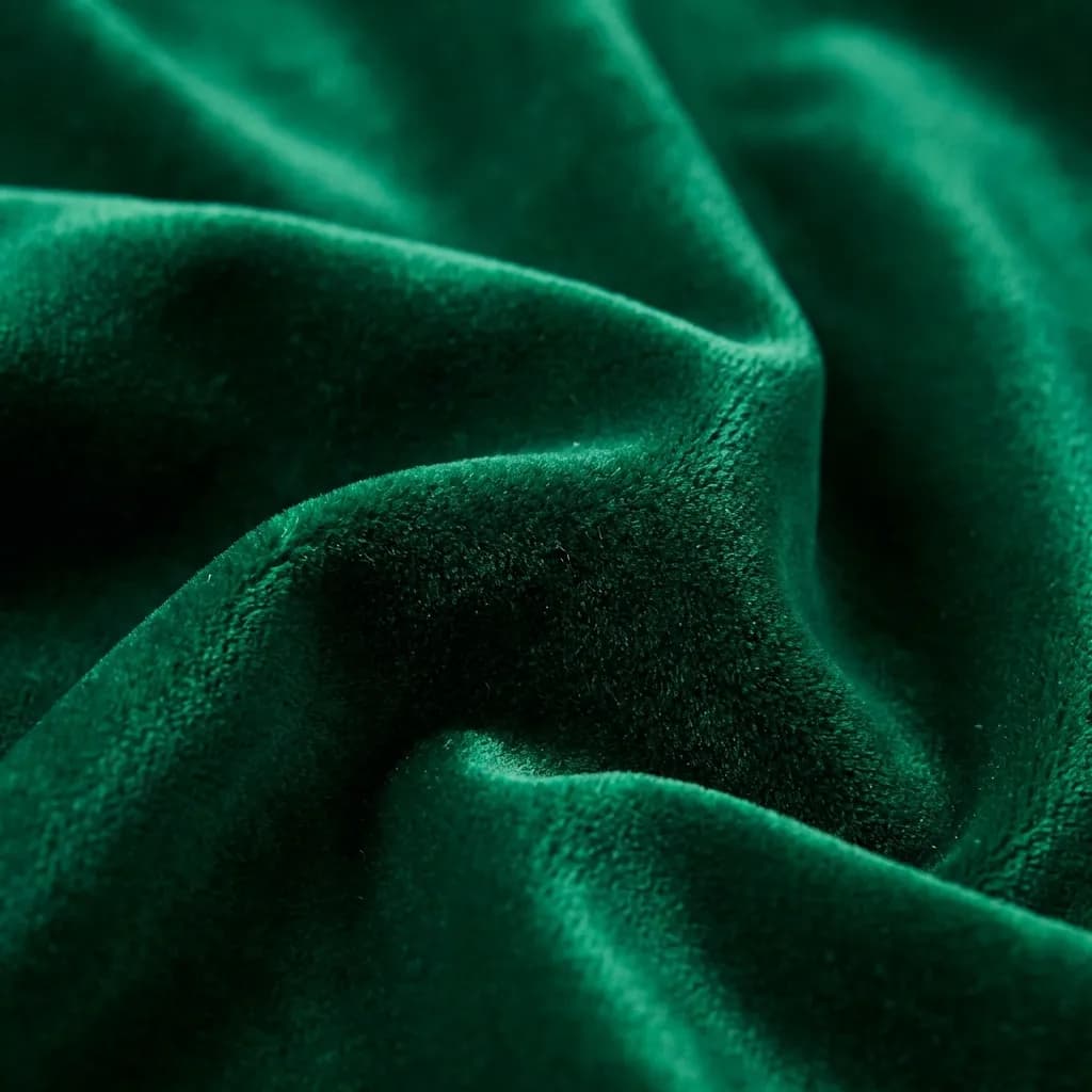 深いエメラルドグリーンのベルベット生地の豪華な質感を捉えたクローズアップ画像です。柔らかく波打つようなドレープが光と影の美しい変化を生み出し、この上なく柔らかな手触りと豊かな色彩を強調しています。非常に心地よく、エレガントで贅沢な雰囲気を醸し出しています。