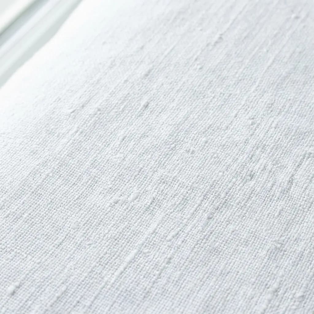 素朴な質感の白い布、おそらくリネンかコットンがクローズアップで捉えられています。織り目の不規則な糸やネップが素材本来の風合いを感じさせ、触れたくなるようなオーガニックな印象です。柔らかな光が生地の凹凸に繊細な陰影をつけ、穏やかで心地よい雰囲気を醸し出しています。
